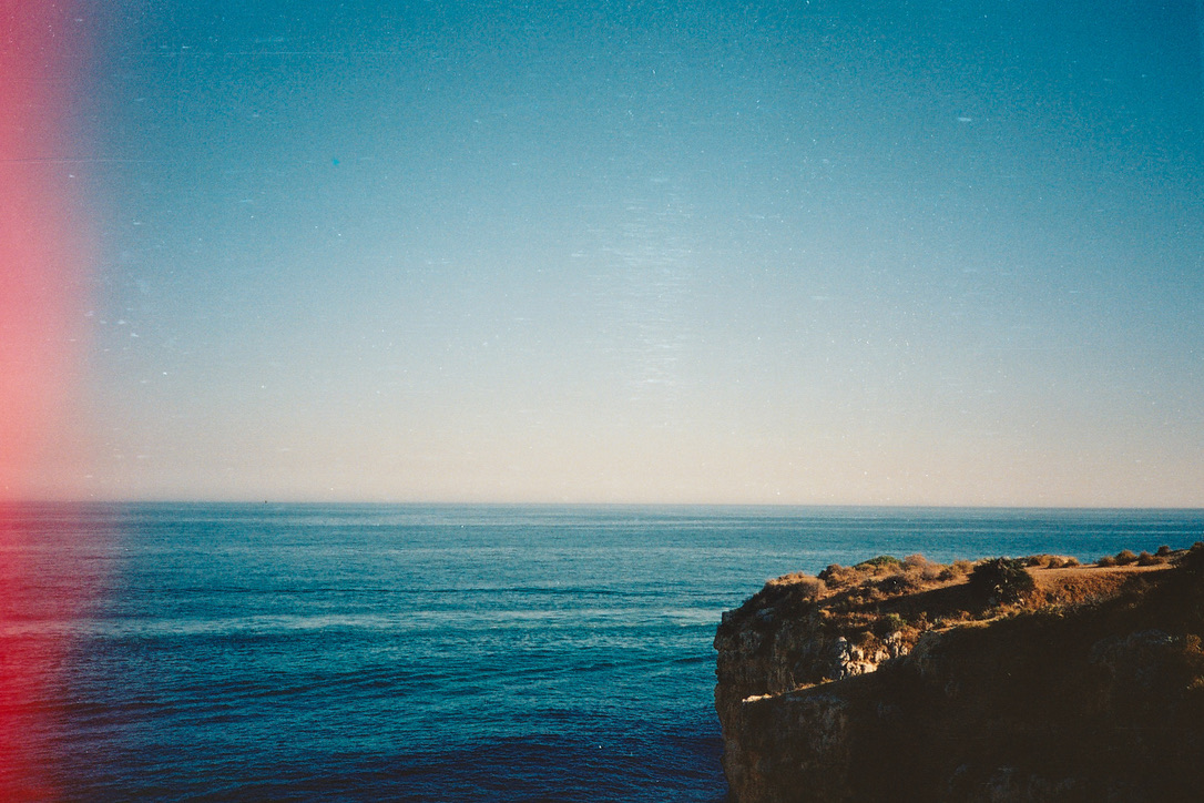 Blue sea beyond a sunlit rocky coast, with a pink light leak at the edge