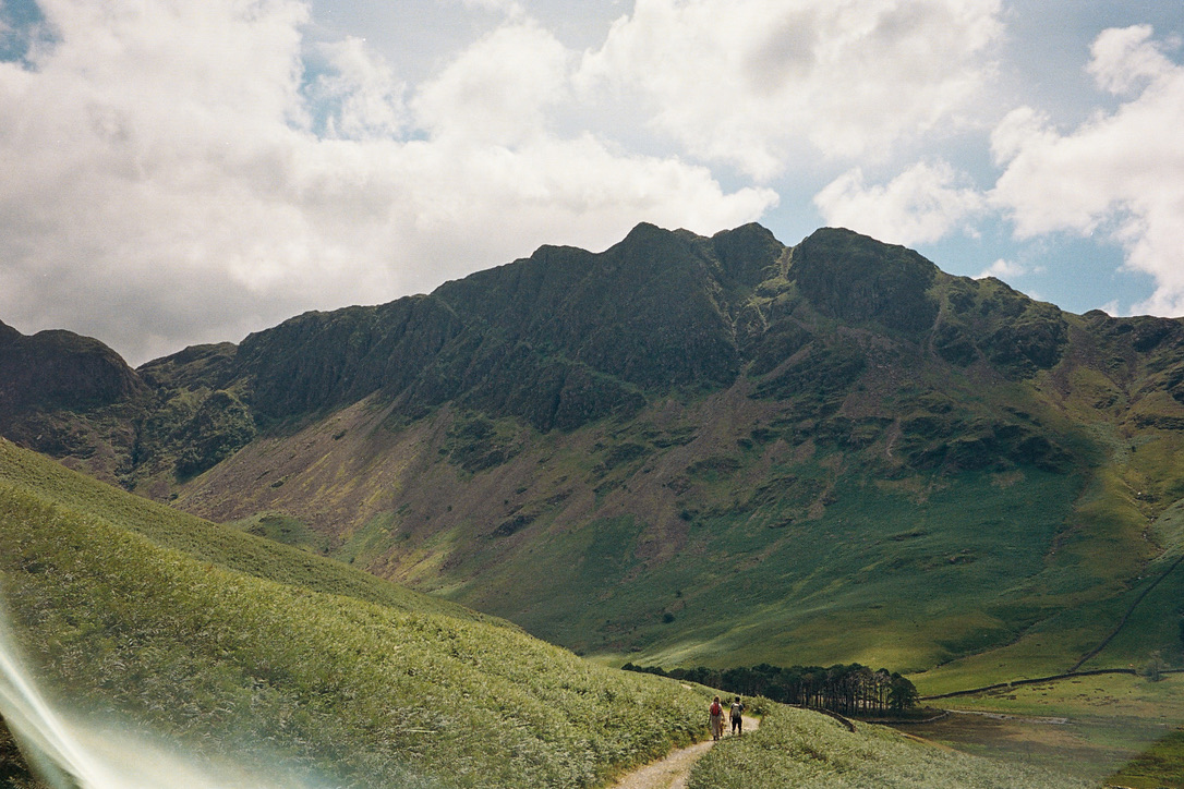 Two walkers on a narrow path through a green mountain valley