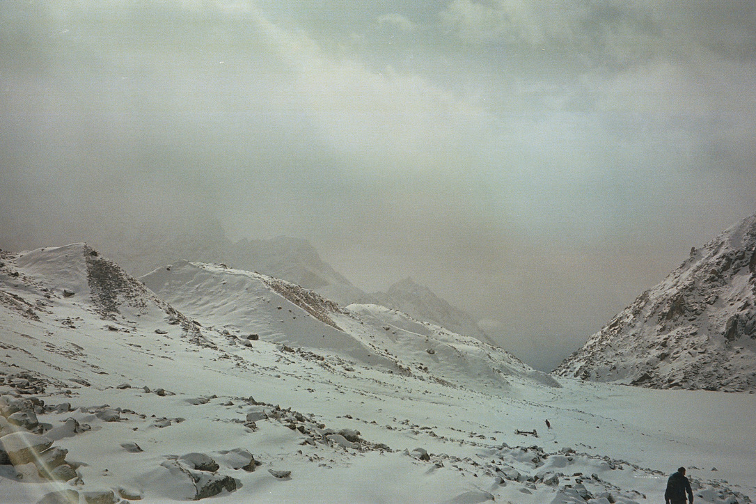 Walkers crossing a broad snow-covered mountain valley under a grey sky