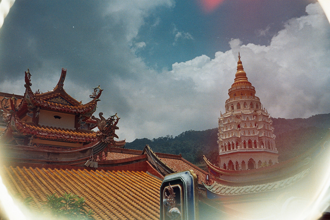 Ornate temple rooftops and a tall pagoda beneath clouds, framed by a film light leak