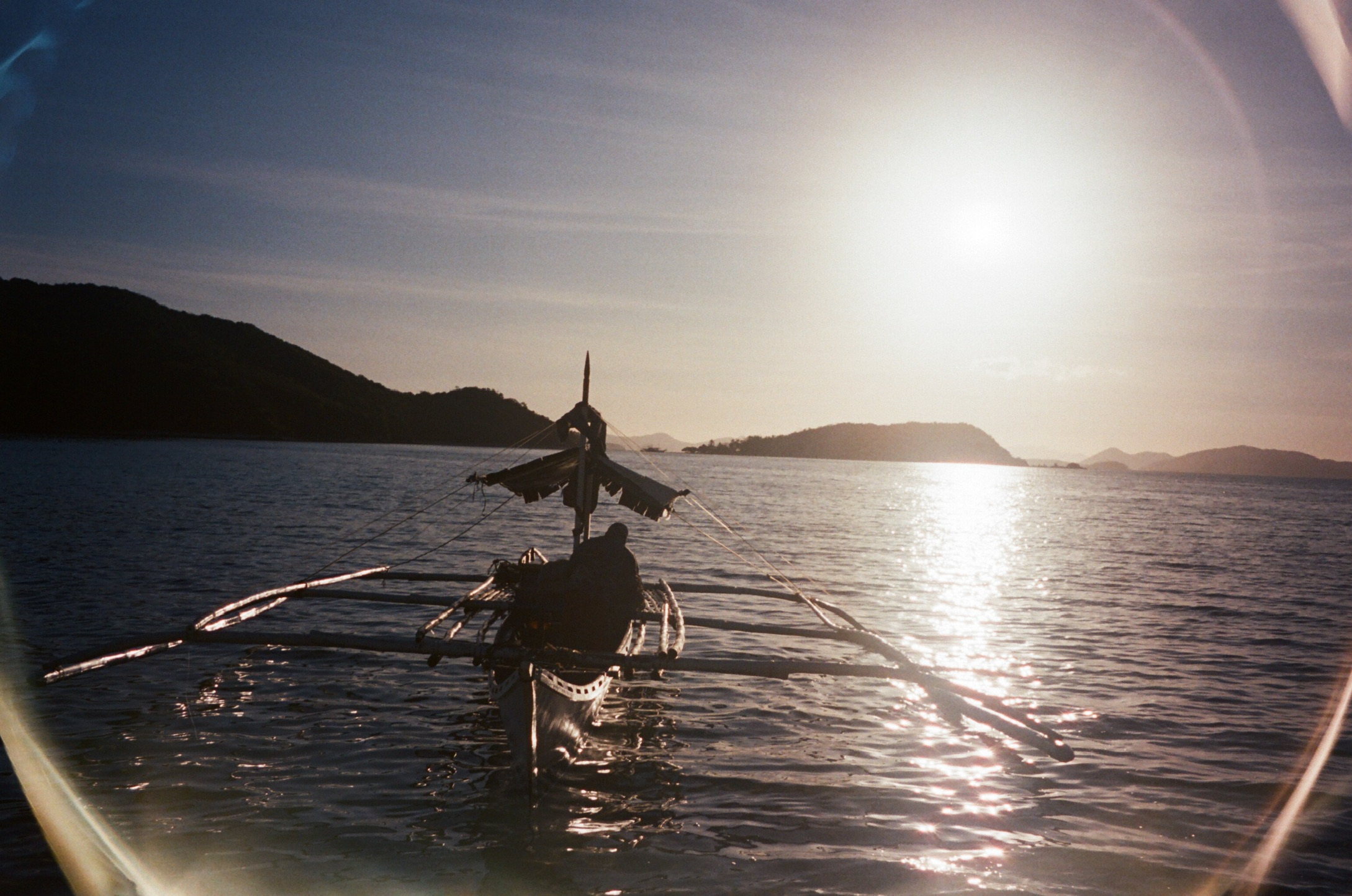 An outrigger boat silhouetted on sunlit water between islands